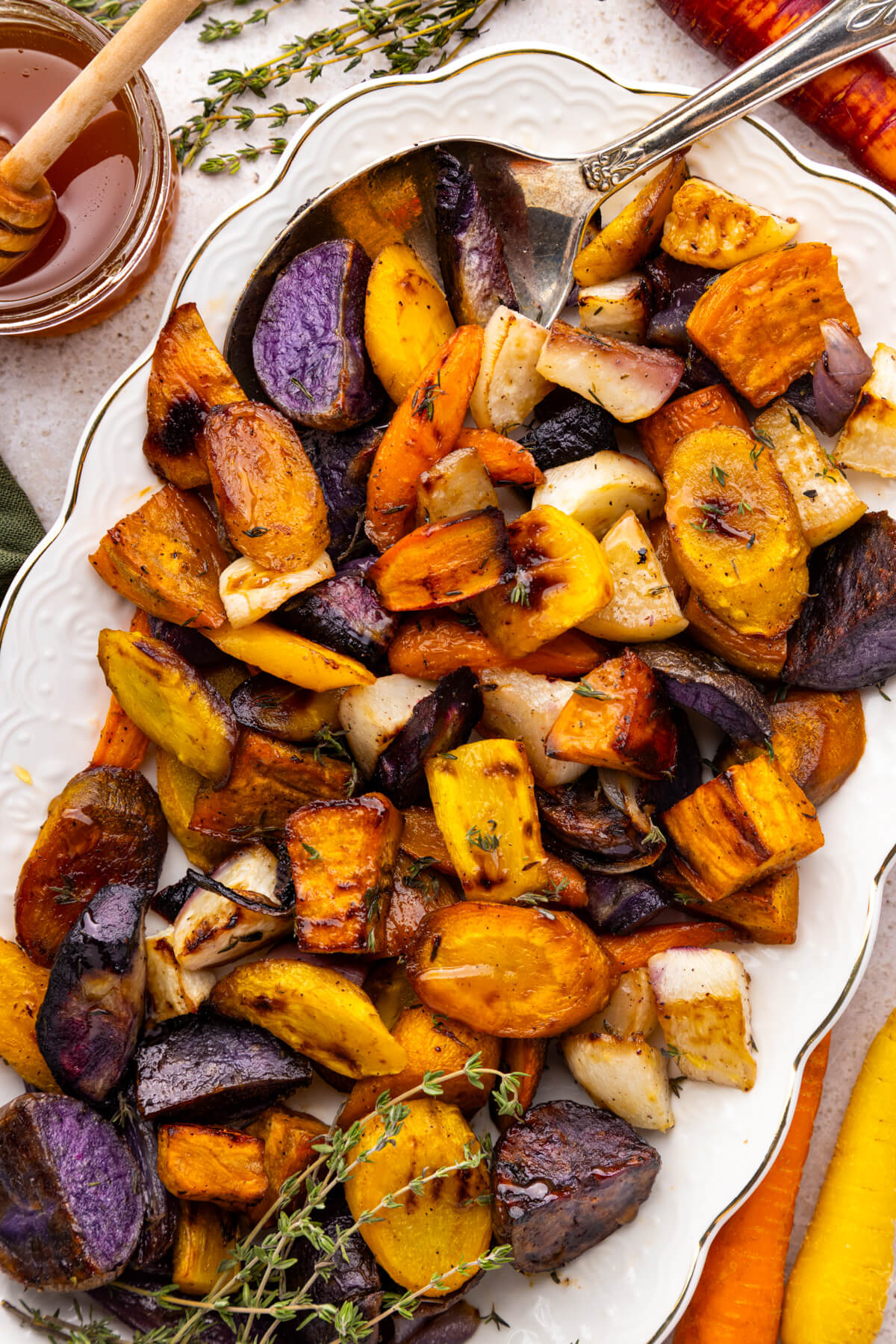 A white platter filled with colourful roasted root vegetables on a dinner table.