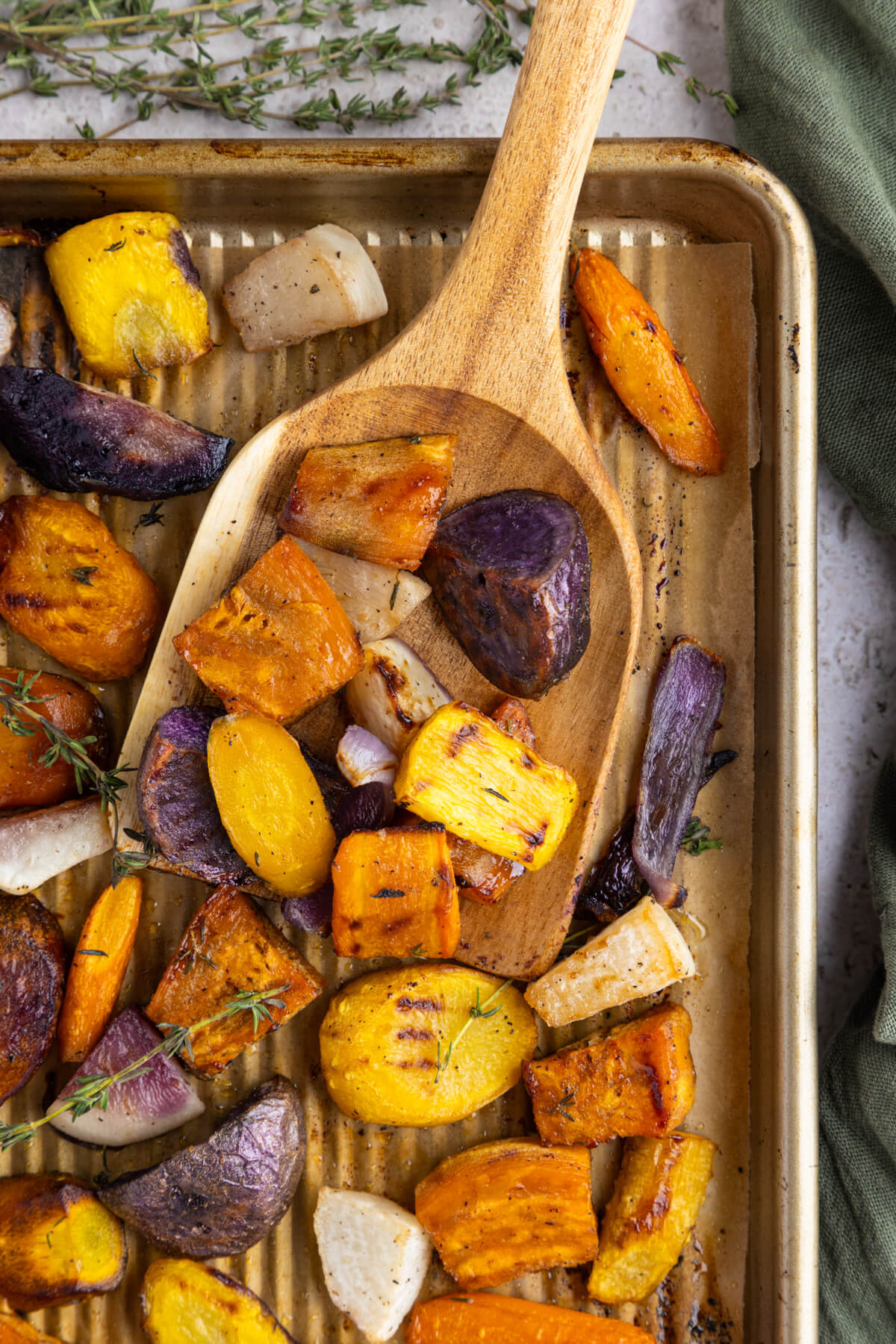 A wooden scoop holding a serving of colourful roasted root vegetables.
