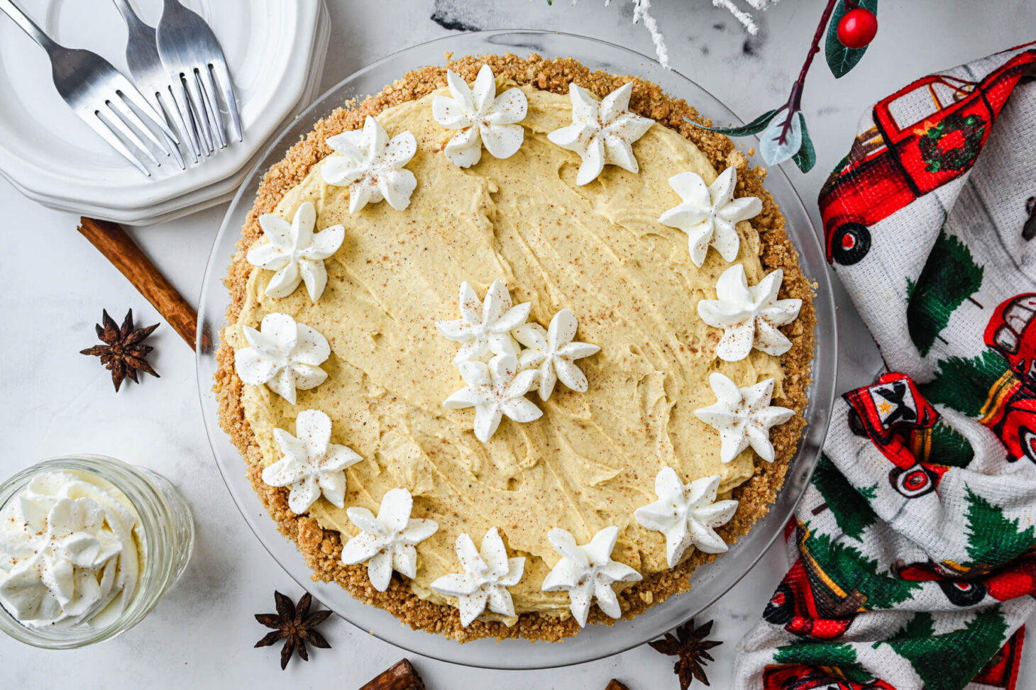 A whole no bake eggnog pie decorated with whipped cream stars on a holiday dinner table.