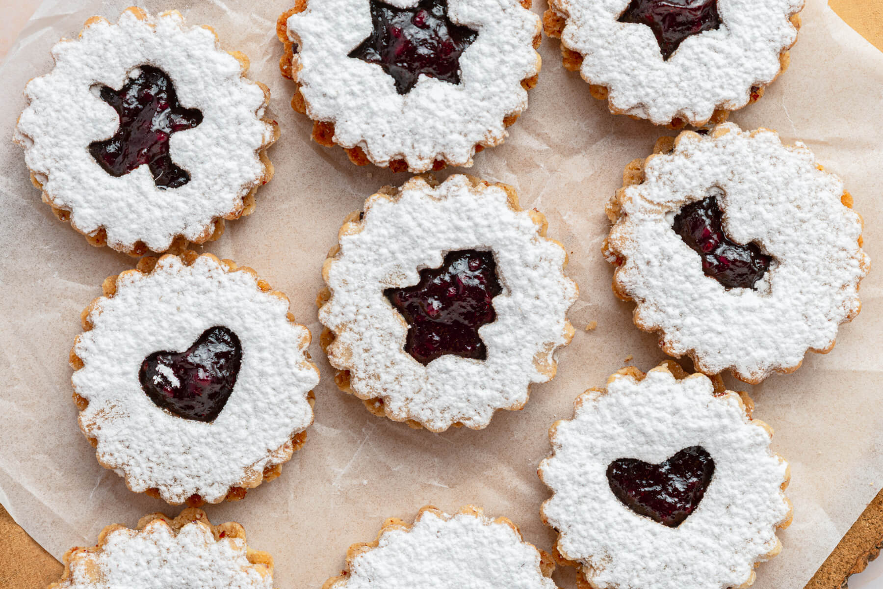 Raspberry Linzer sandwich cookies with bell, star, and heart shaped cut outs dusted in confectioner's sugar.