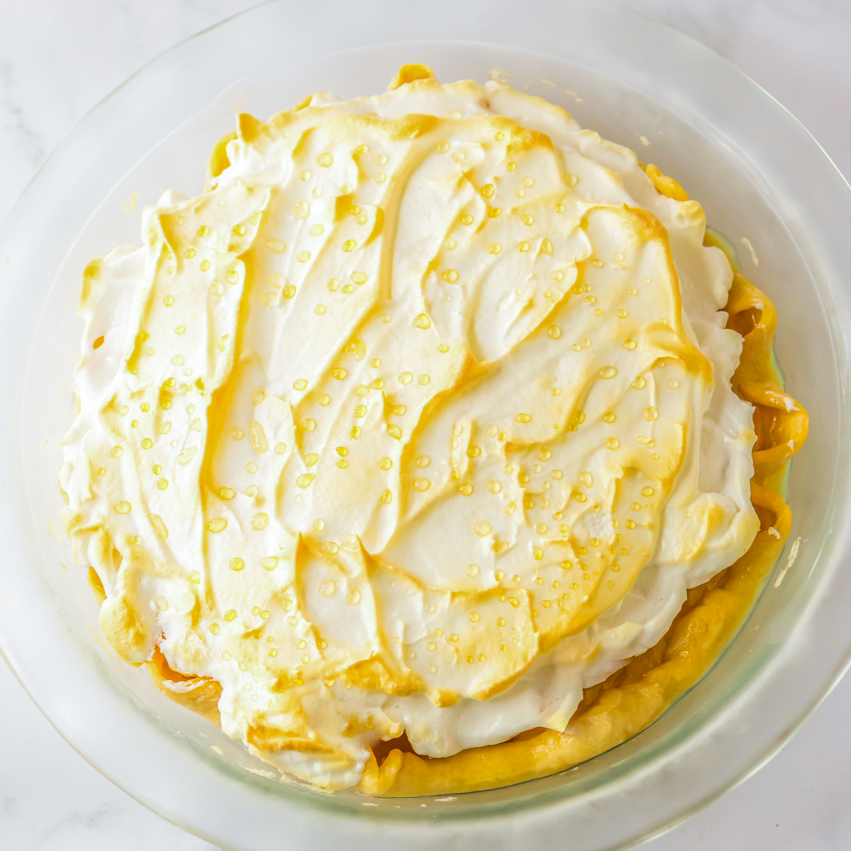 A whole butterscotch pie in a clear pie plate on a white marble table.