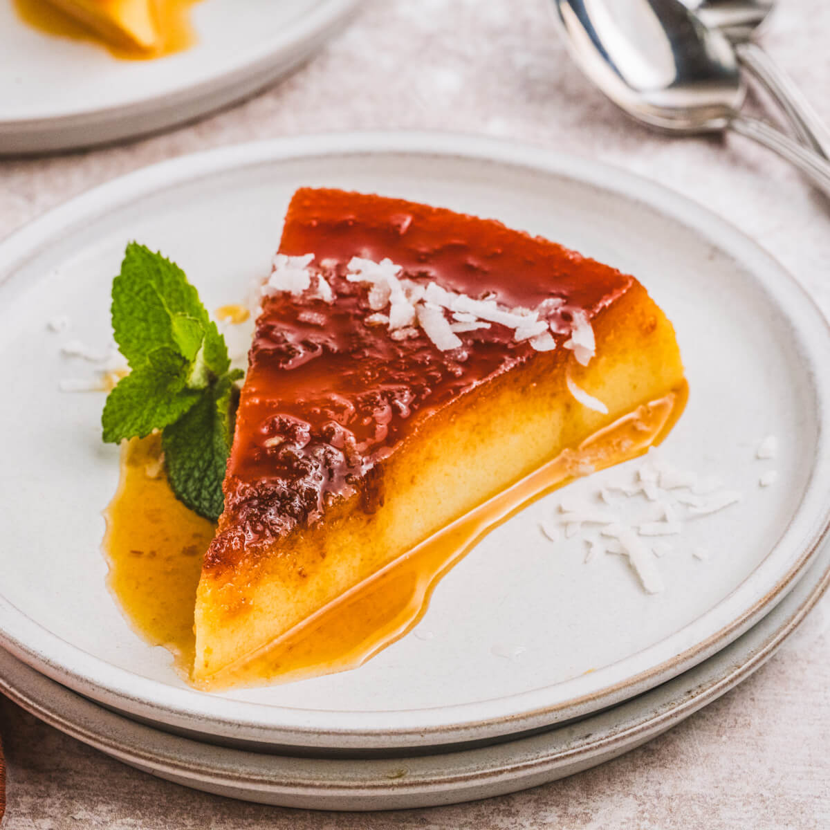 A slice of creamy coconut flan topped with a golden brown caramel and coconut flakes.