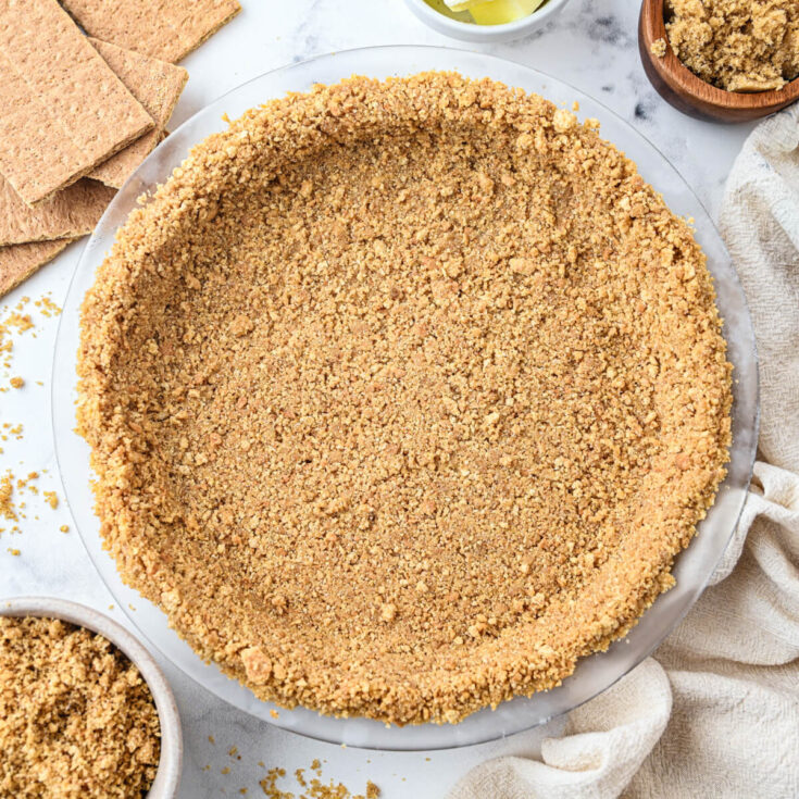 An unfilled 9 inch graham cracker pie crust surrounded by baking ingredients.