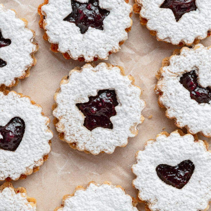 Raspberry Linzer sandwich cookies with bell, star, and heart shaped cut outs dusted in confectioner's sugar.
