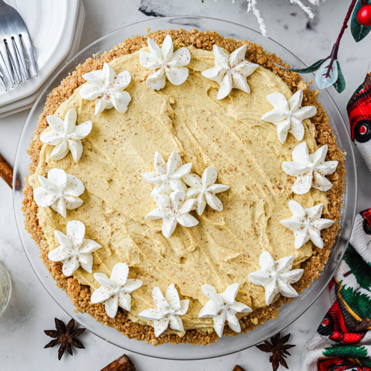 a whole no bake eggnog pie decorated with whipped cream stars on a holiday dinner table.