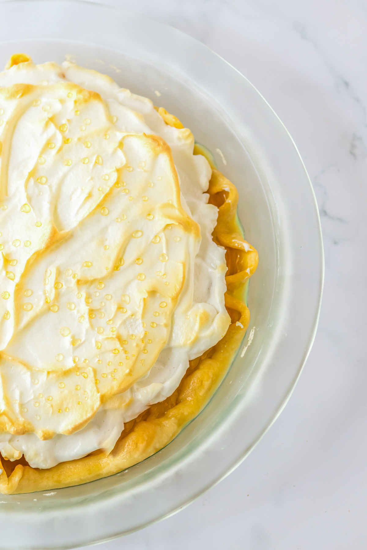 A whole butterscotch pie in a clear pie plate on a white marble table.