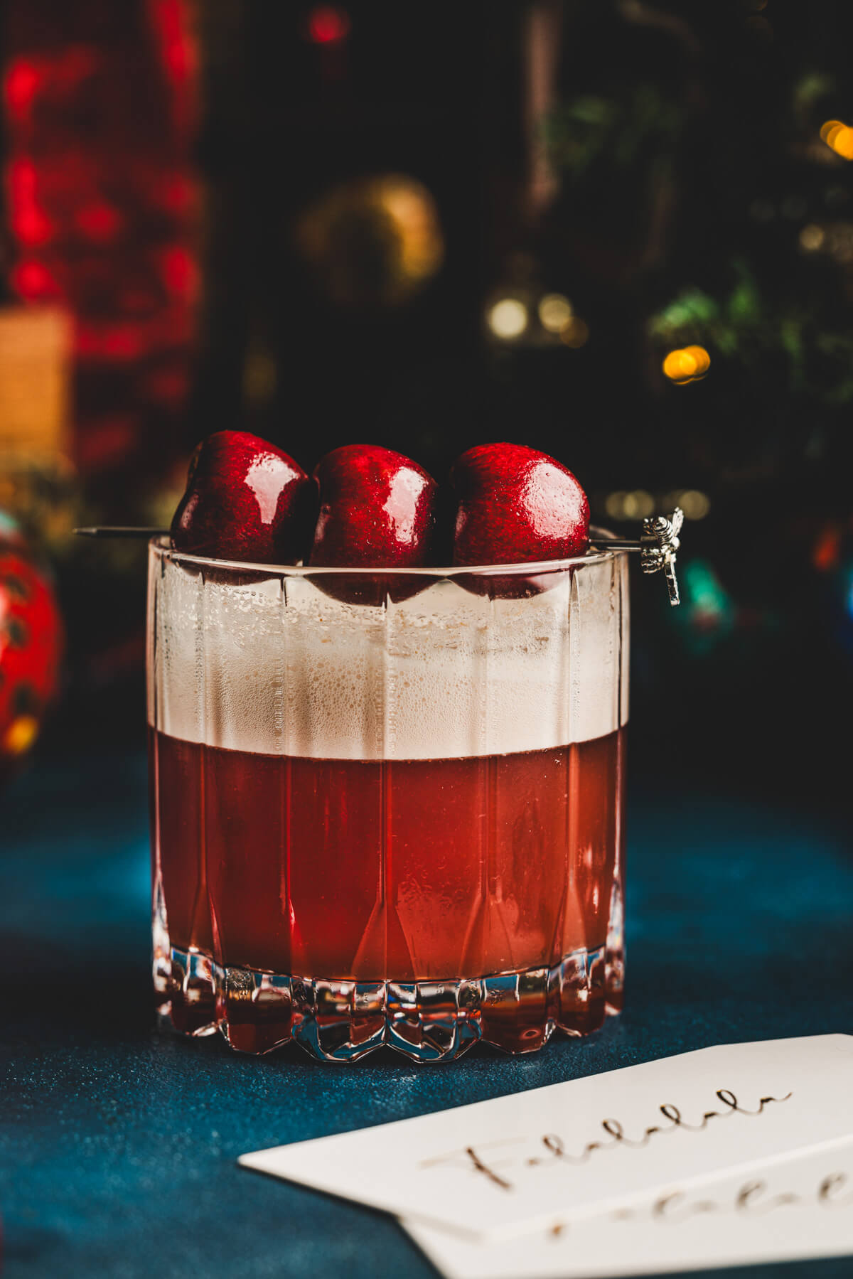 A rocks glass filled with vibrant red amaretto cherry sour cocktail with a top layer of foam and three cherries as garnish.