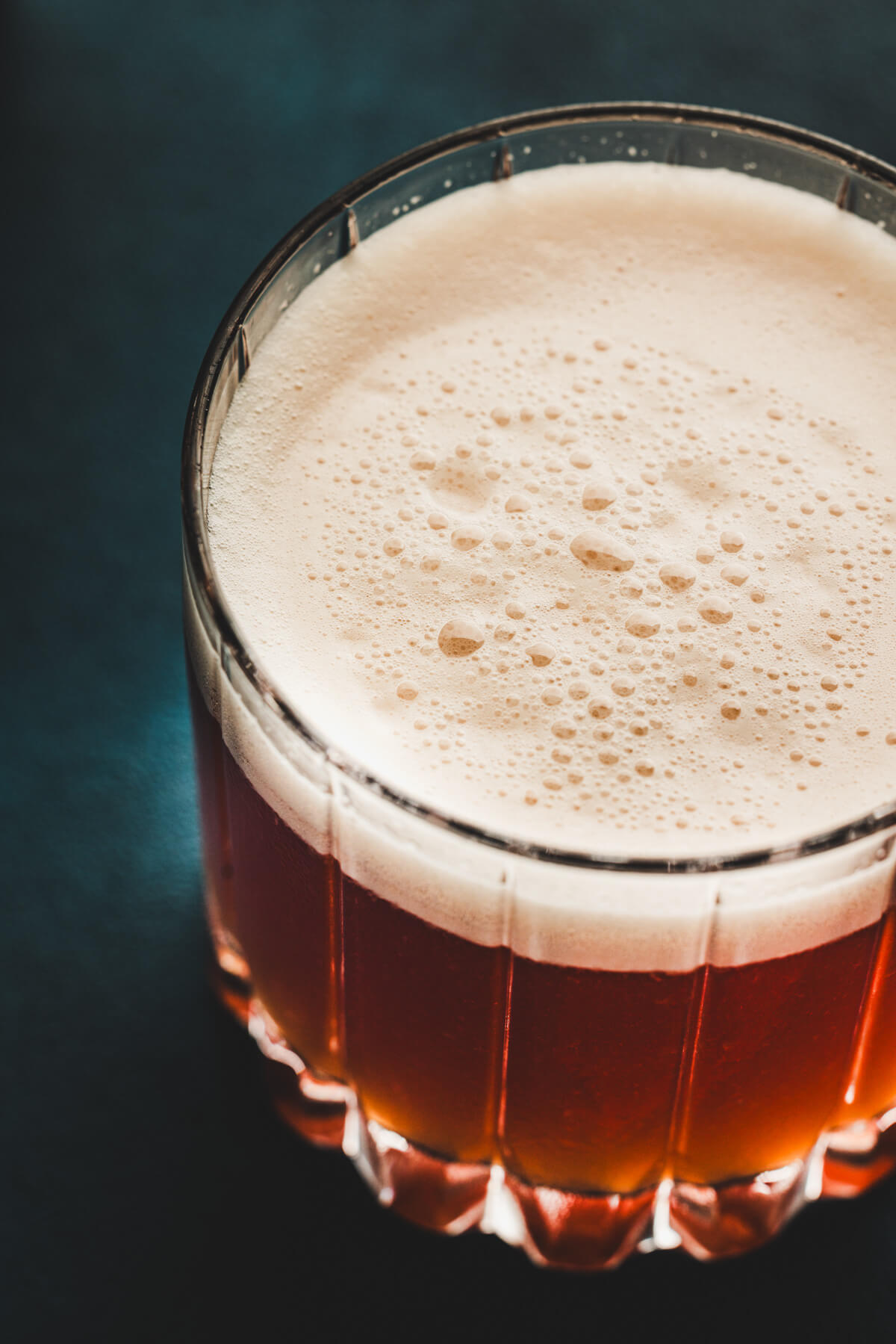 A rocks glass filled with vibrant red amaretto cherry sour cocktail with a generous top layer of foam.