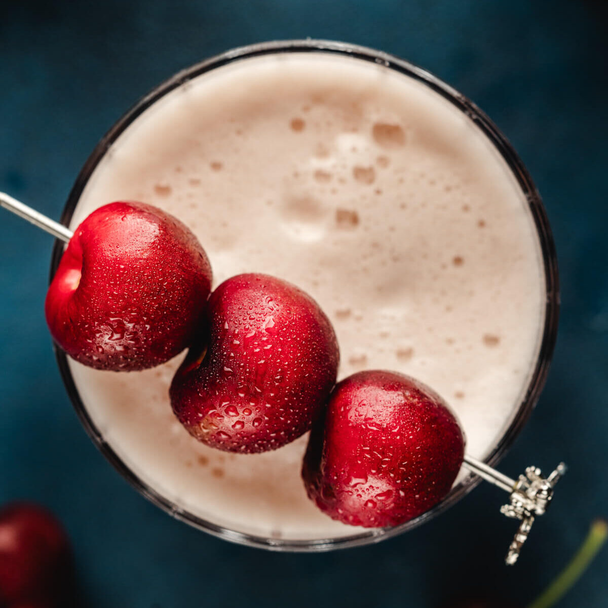 Close up of cherry garnish on top of a cherry amaretto sour cocktail.