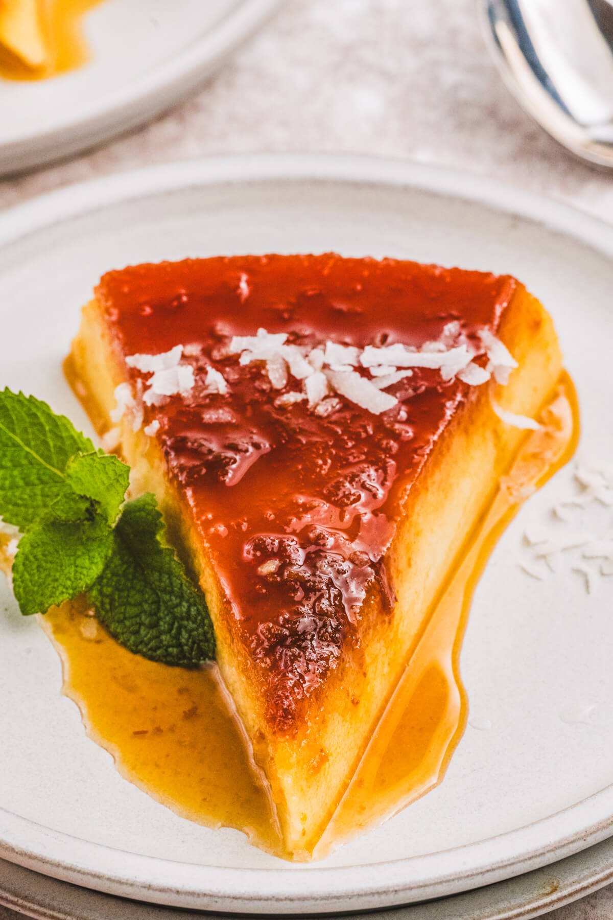 A slice of creamy coconut flan topped with a golden brown caramel and coconut flakes.