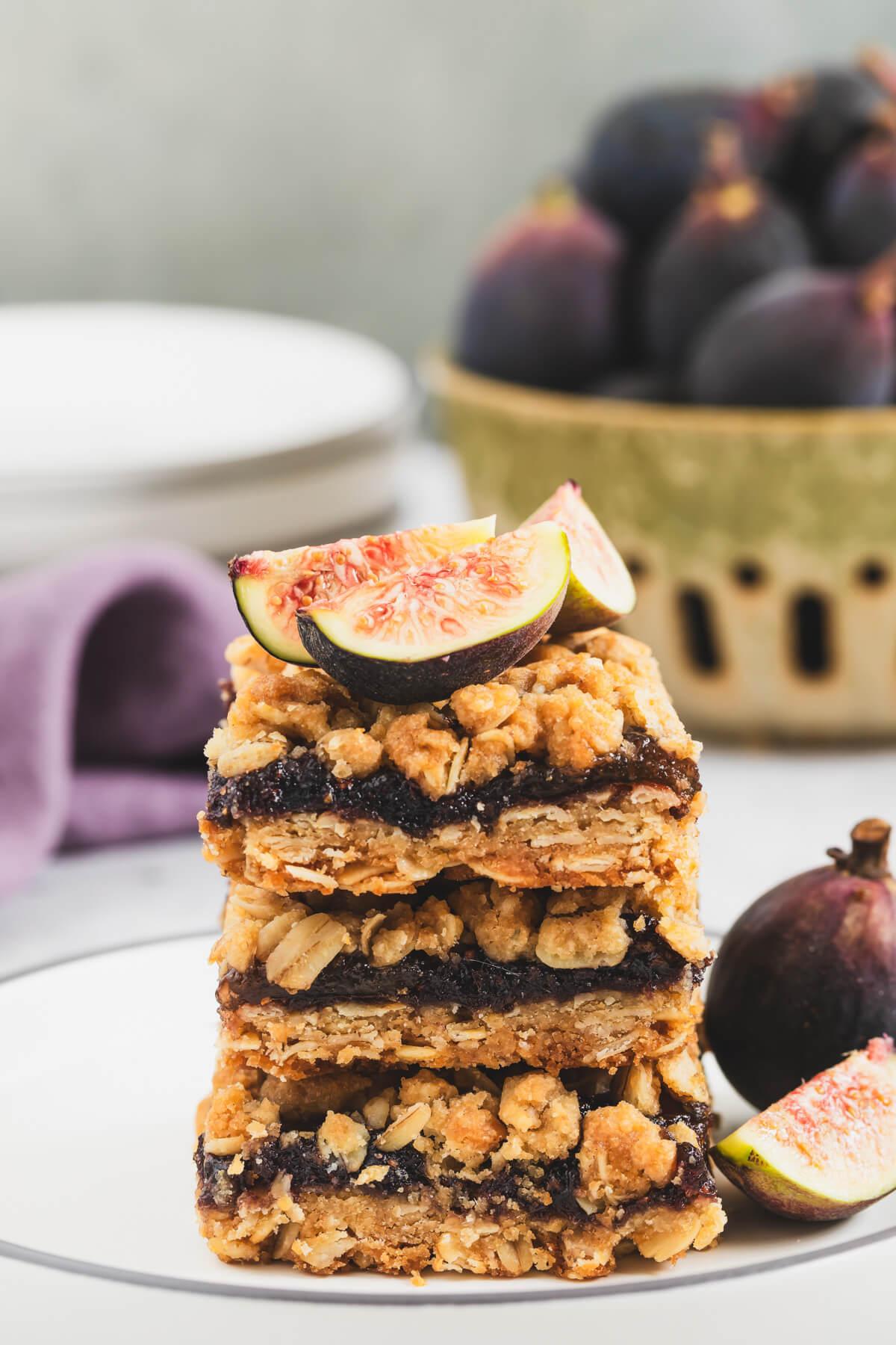A stack of golden baked crumby Fig Bars topped with fresh figs on a white plate.