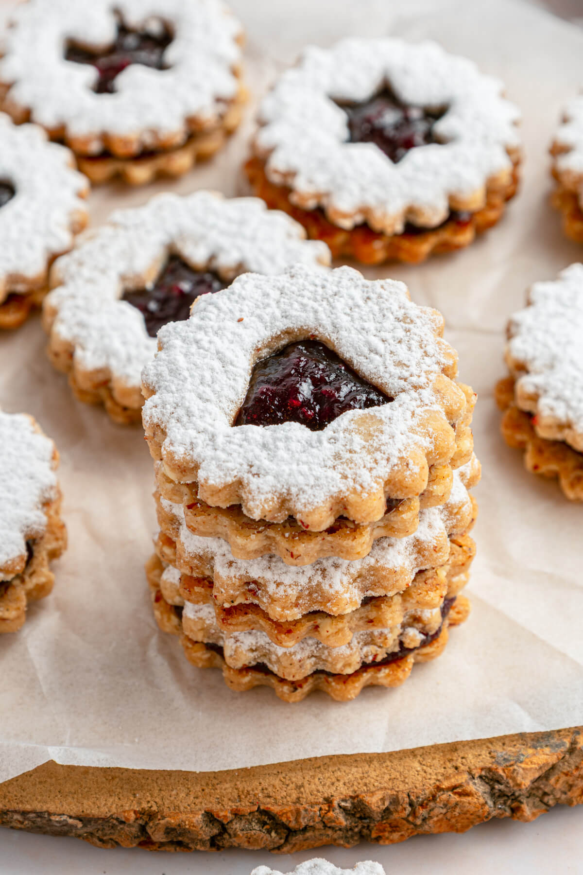 A stack of Raspberry Linzer sandwich cookies with bell, star, and heart shaped cut outs dusted in confectioner's sugar.