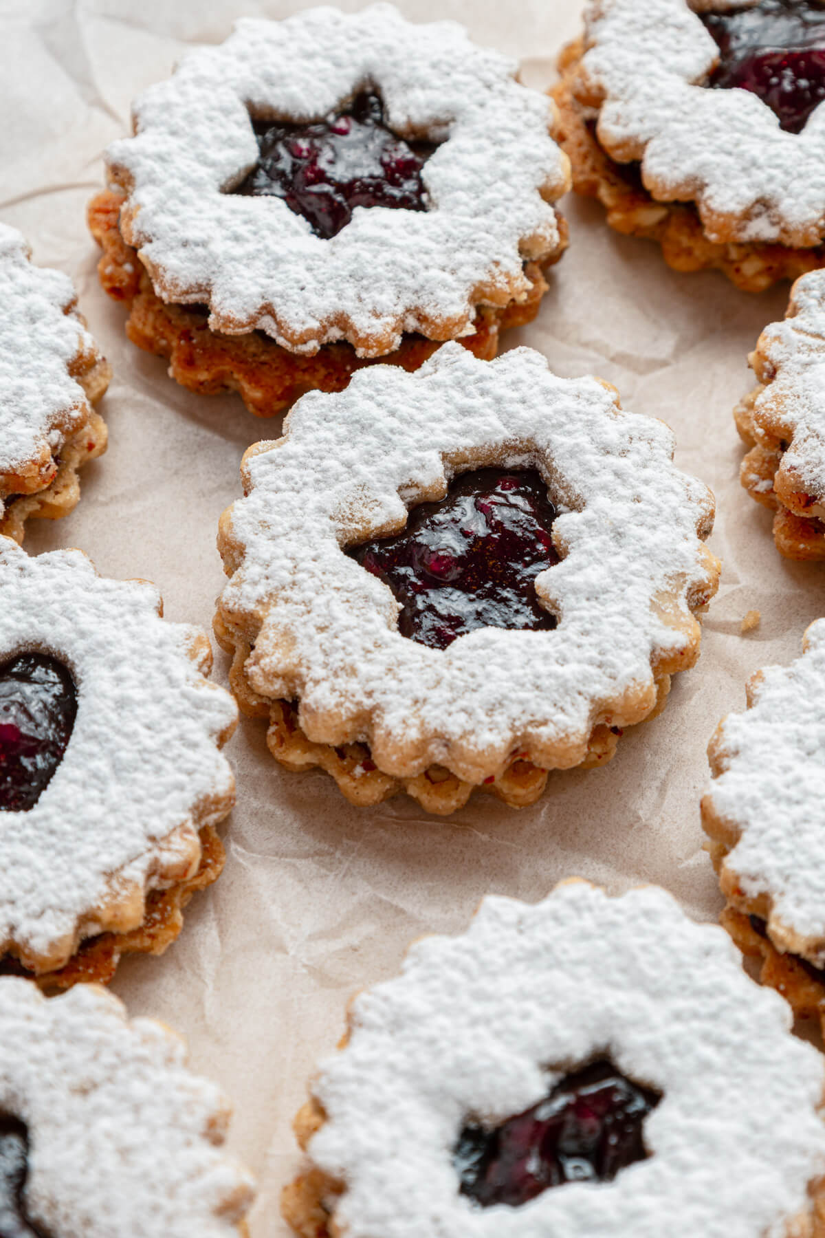 Raspberry Linzer sandwich cookies with bell, star, and heart shaped cut outs dusted in confectioner's sugar.