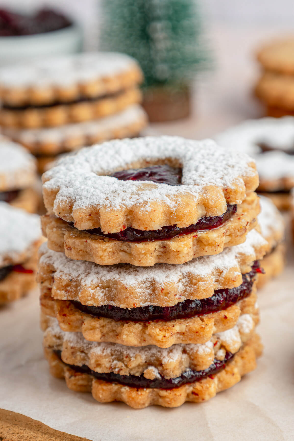 A stack of Raspberry Linzer sandwich cookies with bell, star, and heart shaped cut outs dusted in confectioner's sugar.
