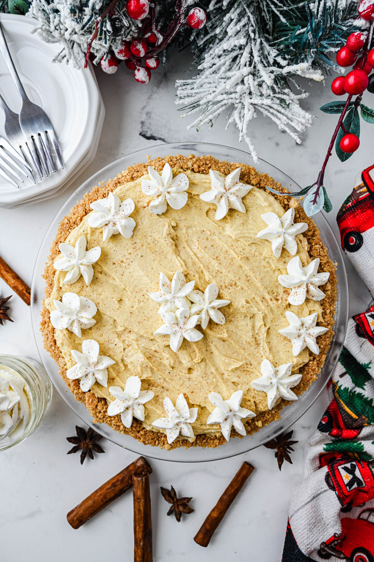 A whole no bake eggnog pie decorated with whipped cream stars on a holiday dinner table.