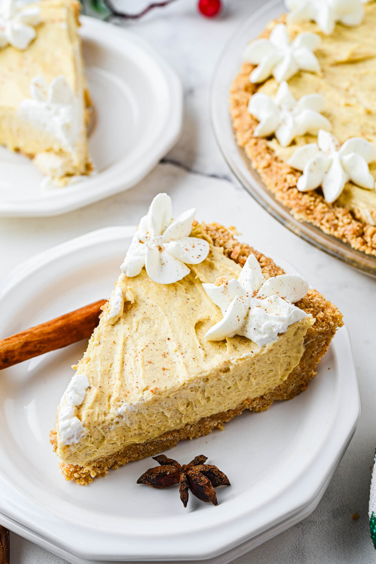 A slice of No Bake Eggnog Pie on a white plate with a cinnamon stick and star anise to decorate.