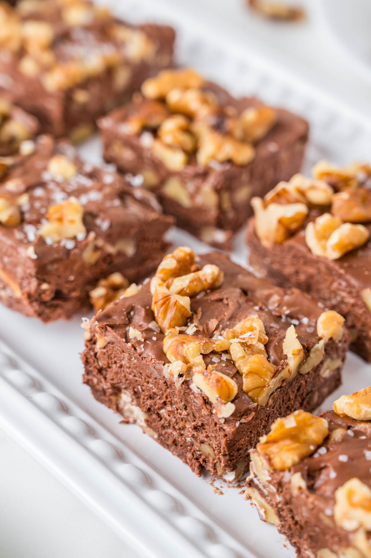 Eight squares of chocolate walnut fudge on a white rectangular plate.