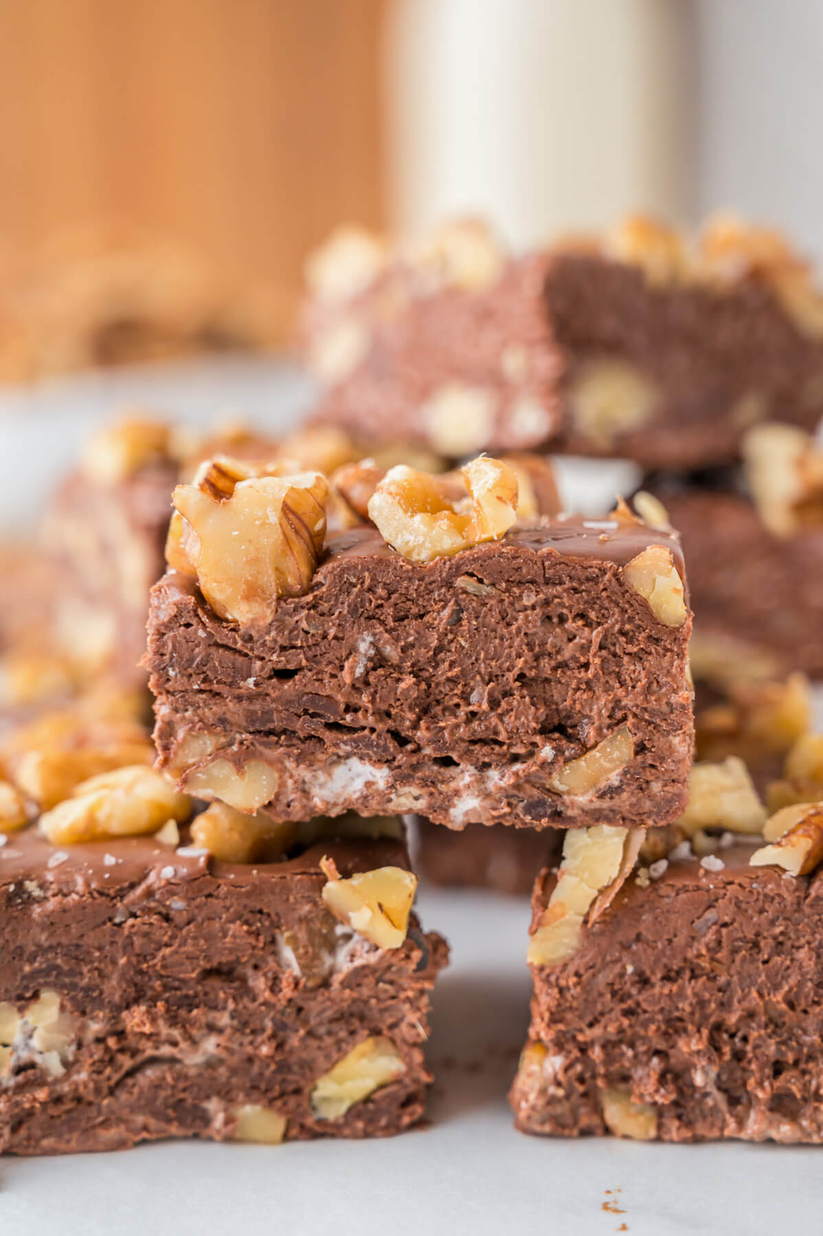 Squares of chocolate walnut fudge stacked into a pyramid in front of more squares of fudge.