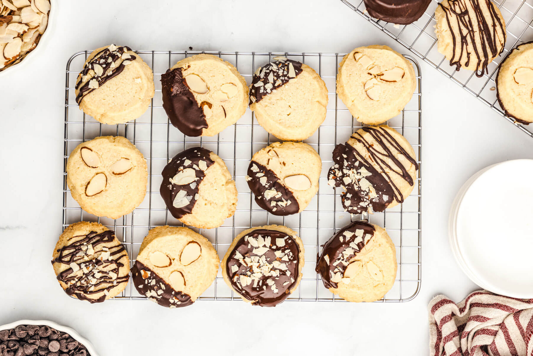 A group of almond shortbread cookies on a cooling rack decorated simply with chocolate glaze or dipped in chocolate accented with sliced and chopped almonds.