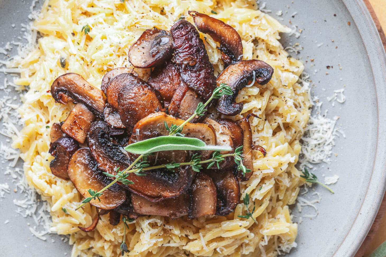 A gray pasta bowl filled with creamy orzo topped with roasted mushrooms and fresh herbs.