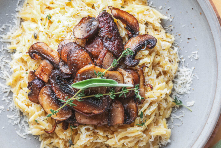 A gray pasta bowl filled with creamy orzo topped with roasted mushrooms and fresh herbs.