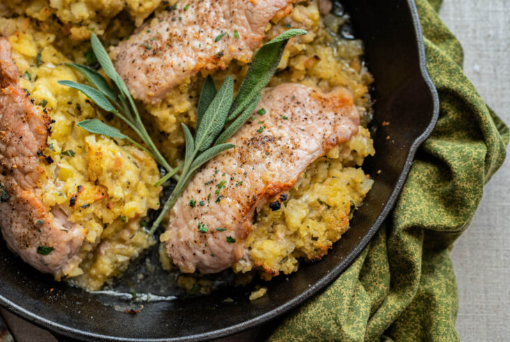 Three perfectly cooked stuffed pork chops in a cast iron skillet garnished with fresh sage.