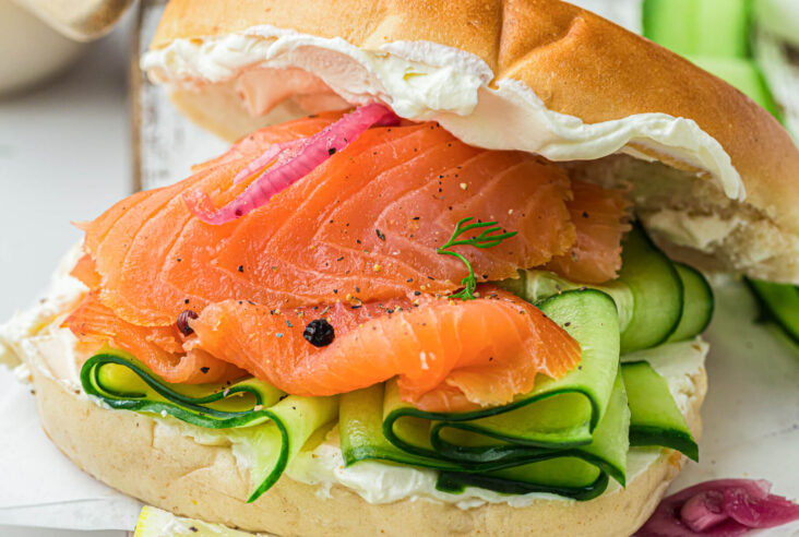 A bagel filled with thin slices of cold smoked salmon, sliced cucumbers, red onions, and cream cheese.