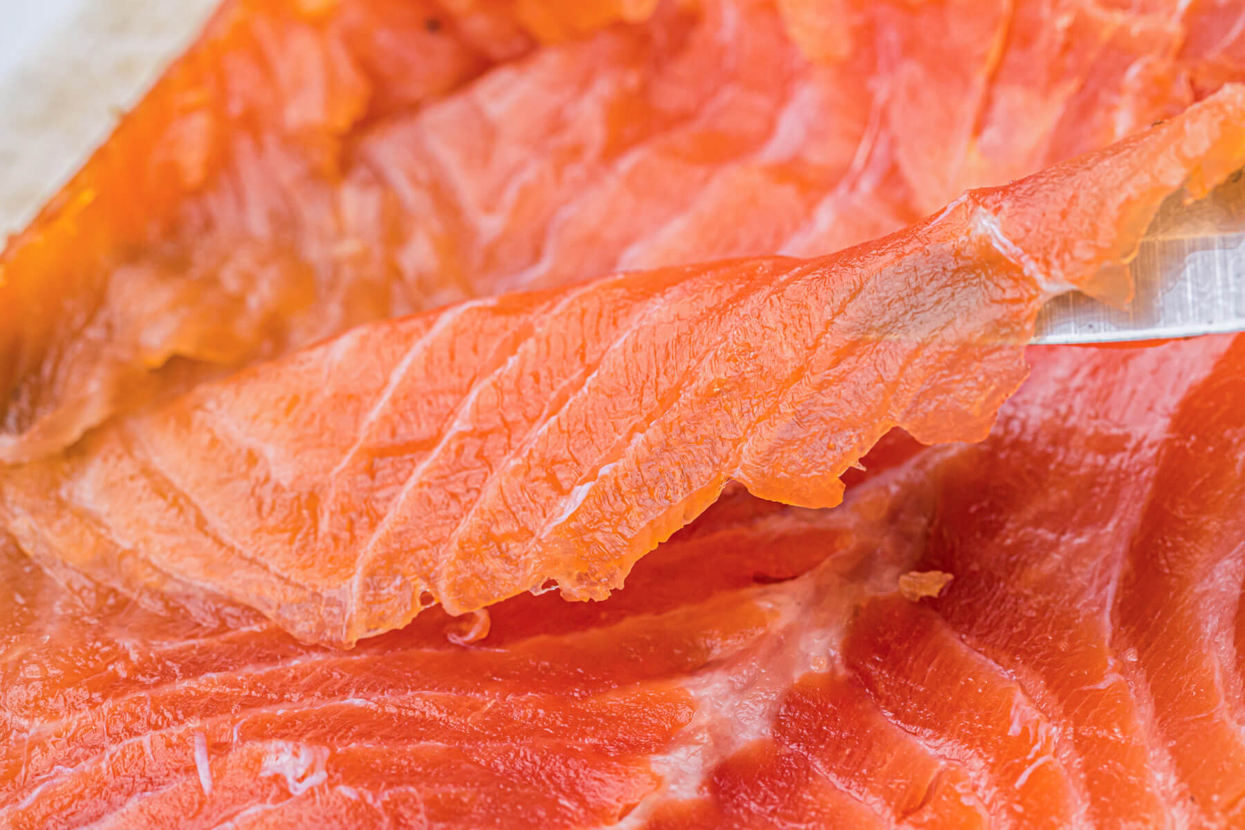 A sharp knife holds up a thin piece off of a whole cold smoked salmon filet.