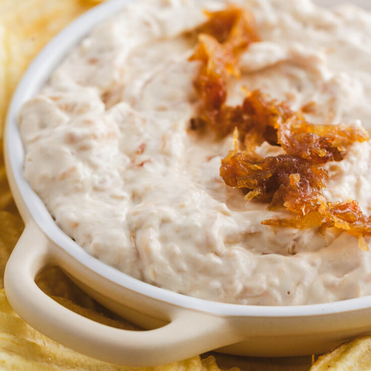 A white bowl filled with creamy white caramelized onion dip topped with golden brown caramelized onions.