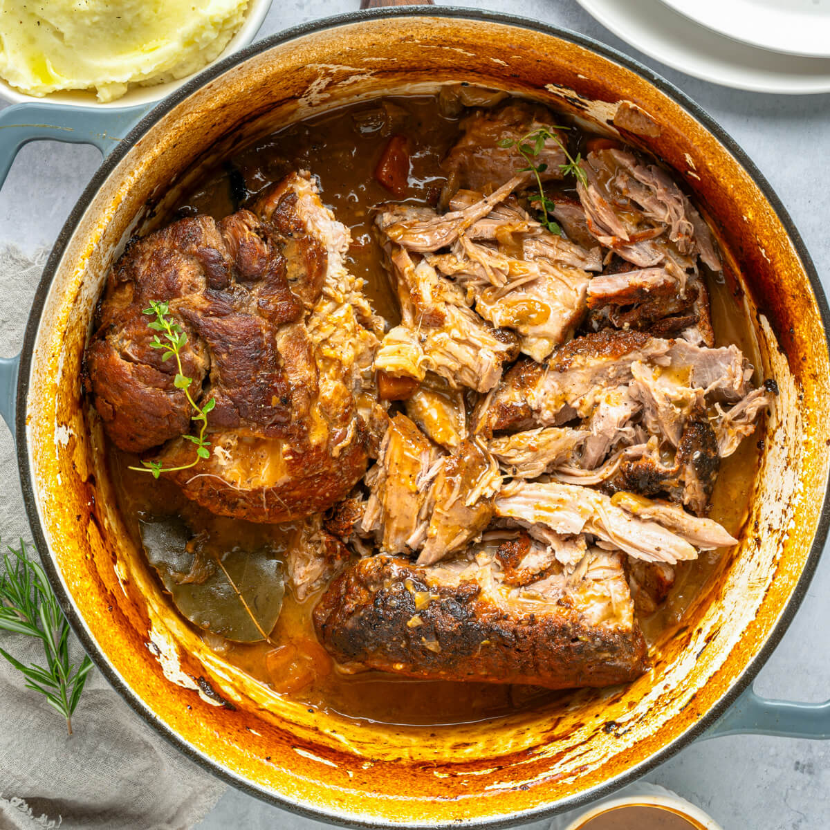 A Dutch oven containing fork tender braised pork shoulder in braising liquid.