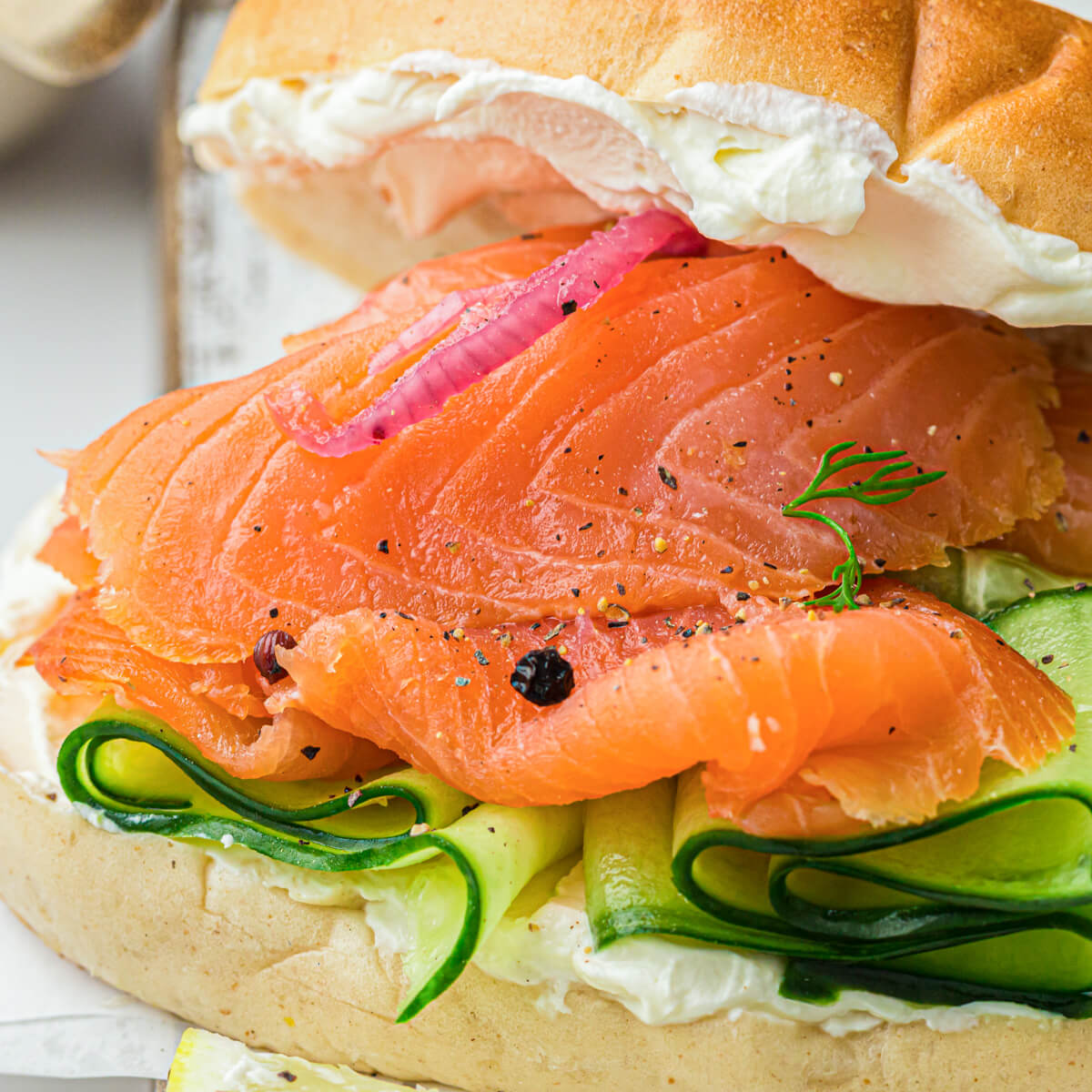 A bagel filled with thin slices of cold smoked salmon, sliced cucumbers, red onions, and cream cheese.