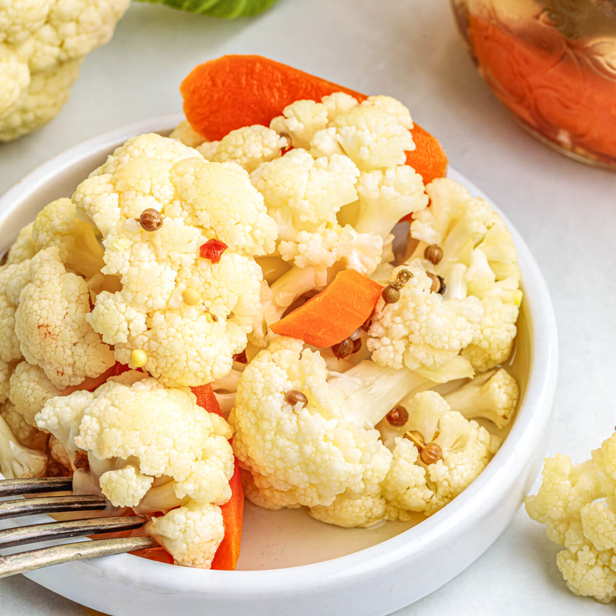 A small white dish containing quick pickled cauliflower with a few carrots and pickling spices.