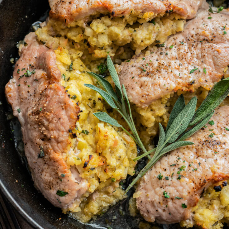 Three perfectly cooked stuffed pork chops in a cast iron skillet garnished with fresh sage.