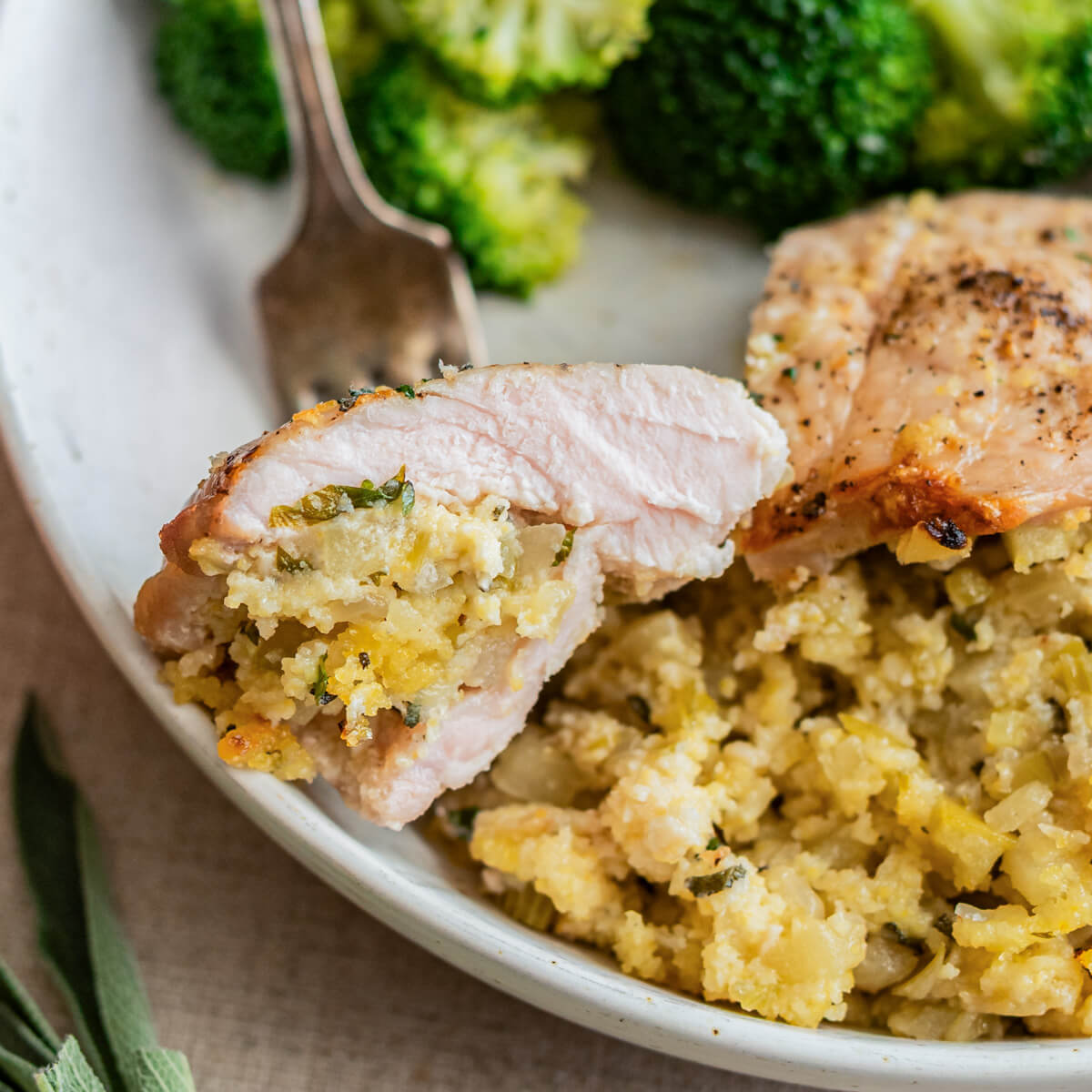 A fork containing a slice of stuffed pork chop floats above a dinner plate.
