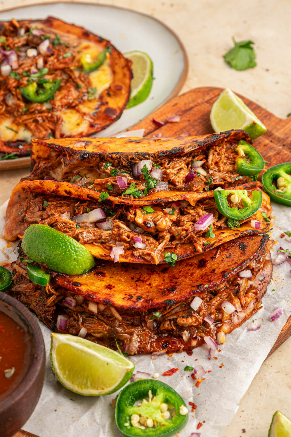 A plate of beefy Birria Tacos garnished with bright green cilantro, chopped onions, jalapeños and lime wedges.