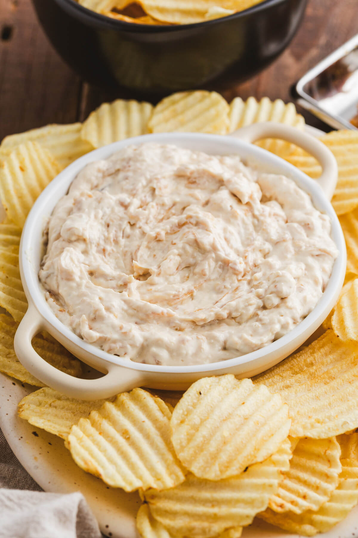 A white bowl filled with creamy white caramelized onion dip surrounded by ripple potato chips.