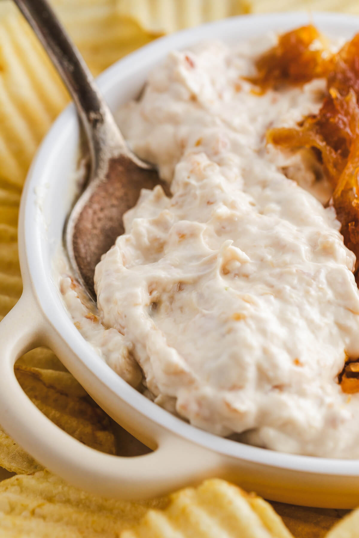 A spoon scoops a generous portion of caramelized onion dip out of a white dip bowl.