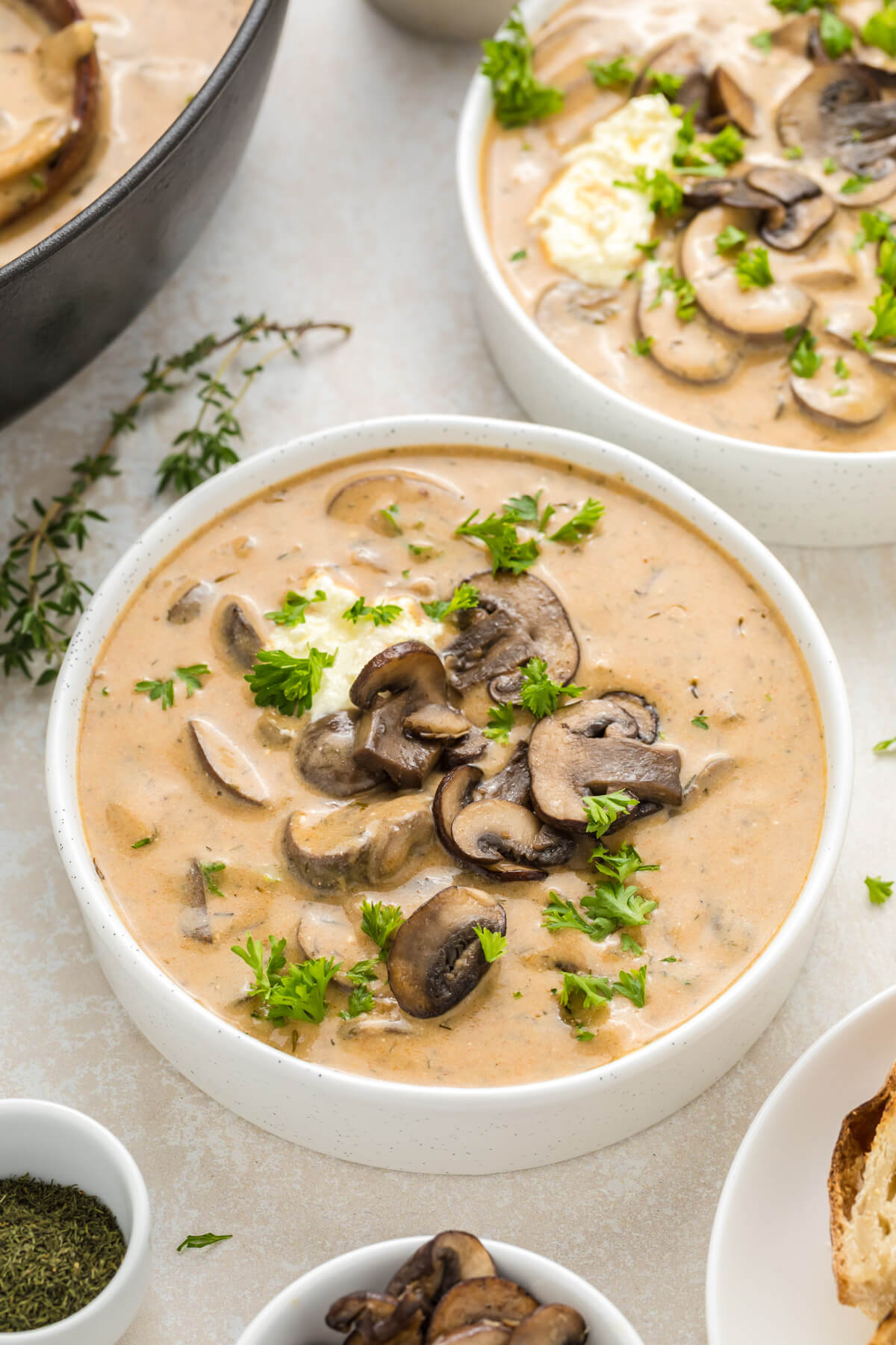 A white soup bowl full of rich creamy Hungarian Mushroom Soup topped with vibrant green herbs on a dining table.