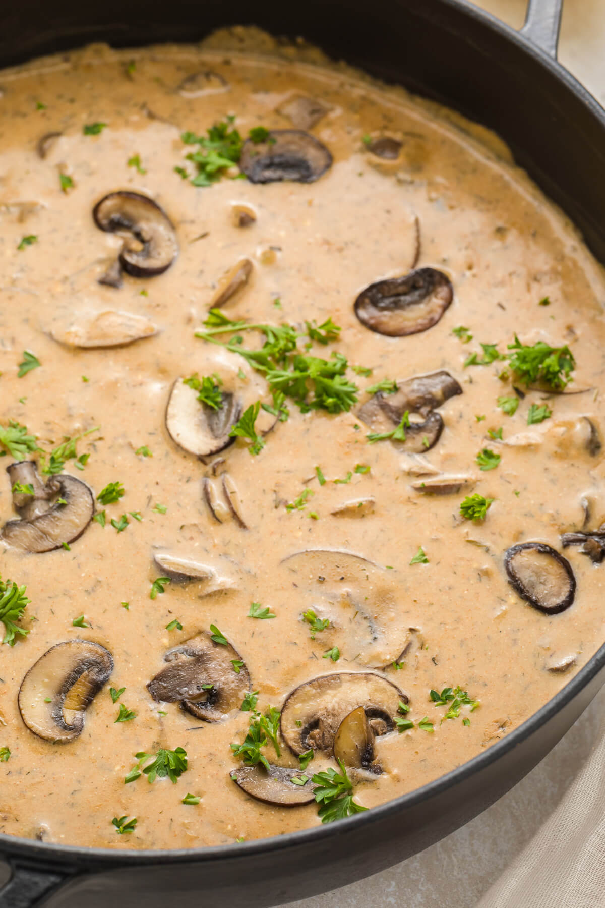 A black Dutch oven full of rich creamy Hungarian Mushroom Soup topped with vibrant green herbs.