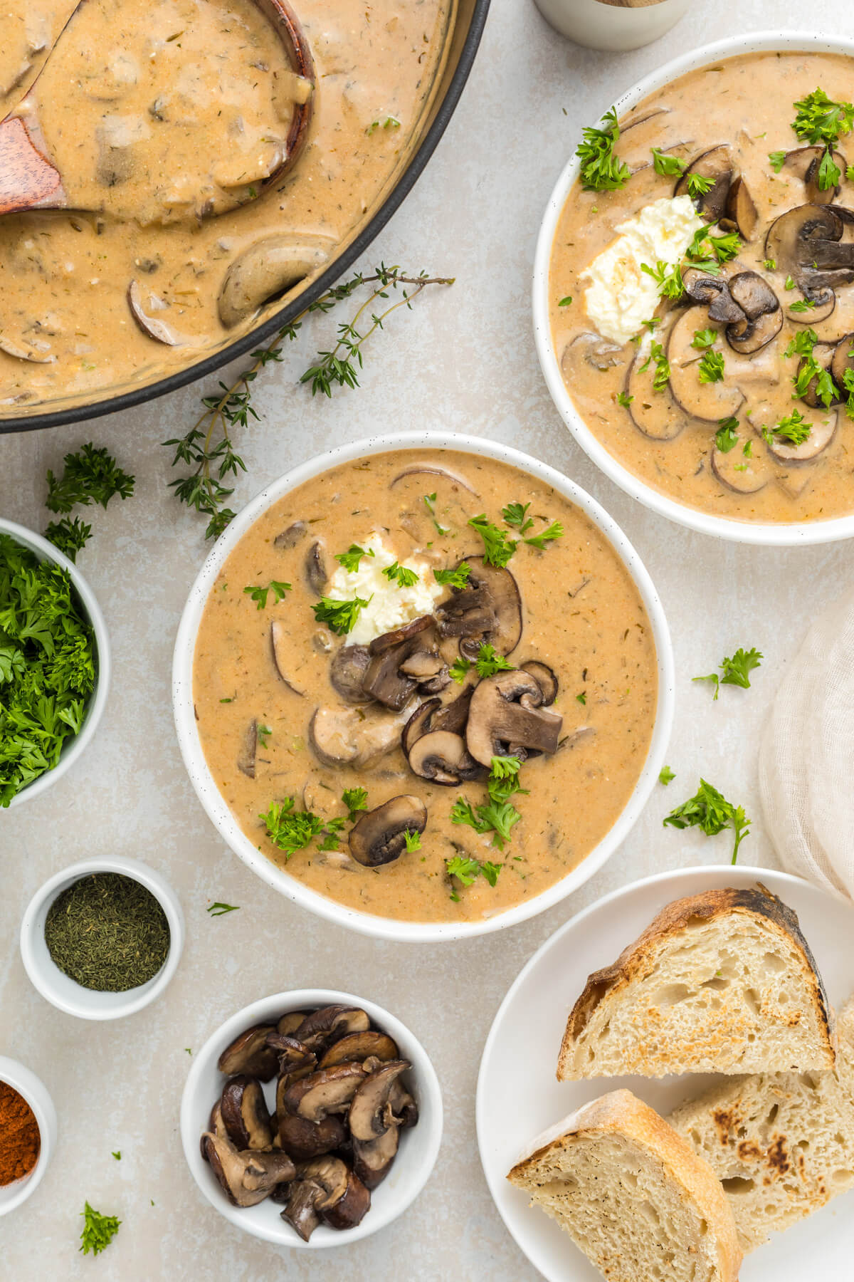 Two white soup bowls full of rich creamy Hungarian Mushroom Soup topped with vibrant green herbs on a dining table.
