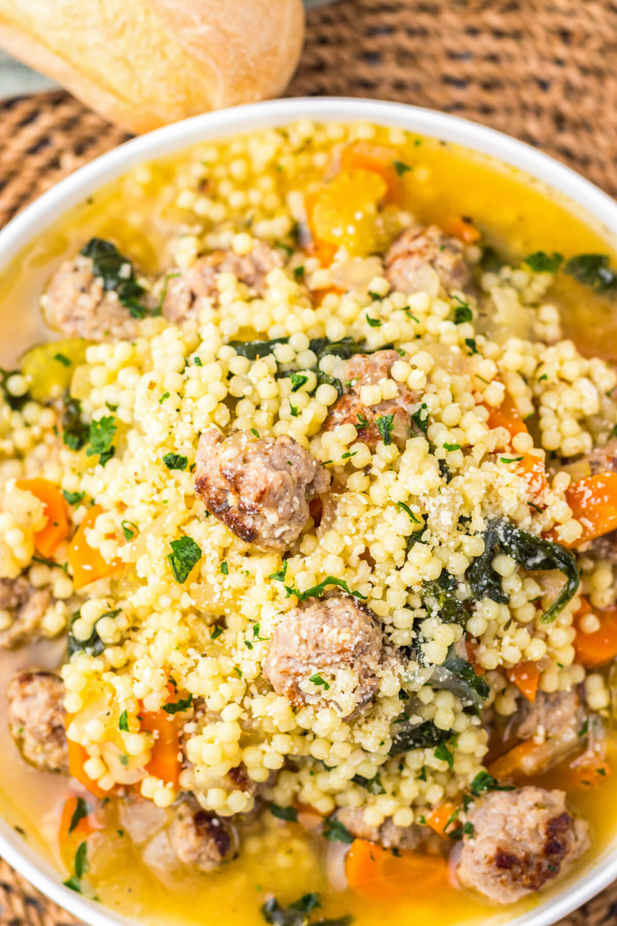 A white soup bowl filled with chicken broth, carrots, spinach, acini di pepe pasta, and Italian meatballs.