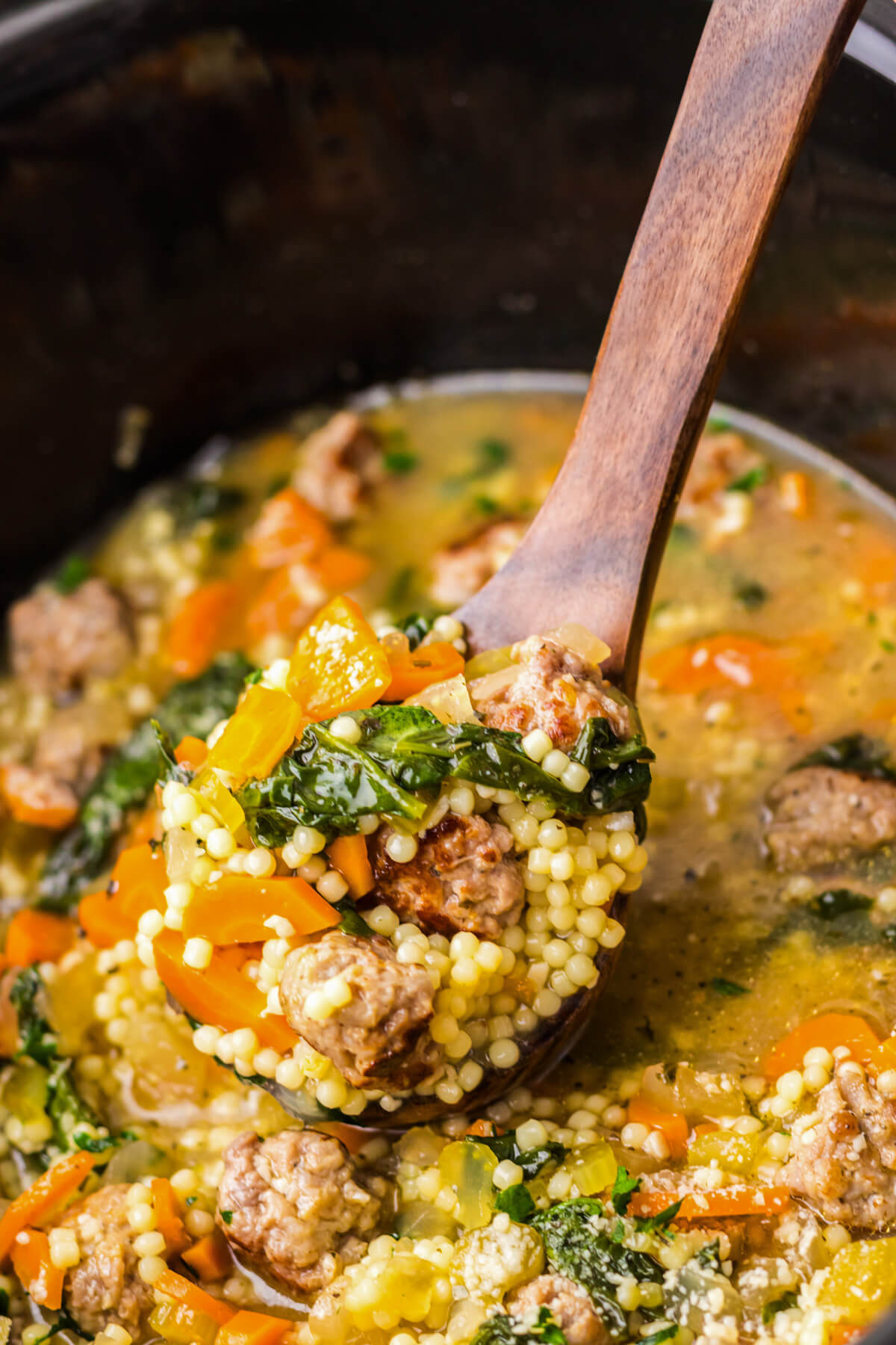A wooden ladle containing a serving of slow cooker Italian wedding soup.