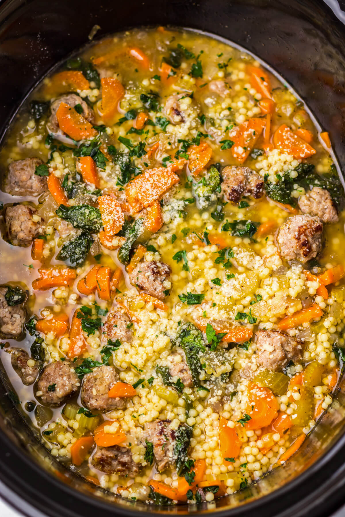 Italian Wedding soup with rich yellow broth containing carrots, spinach, meatballs, and acini di pepe pasta in a black slow cooker insert.