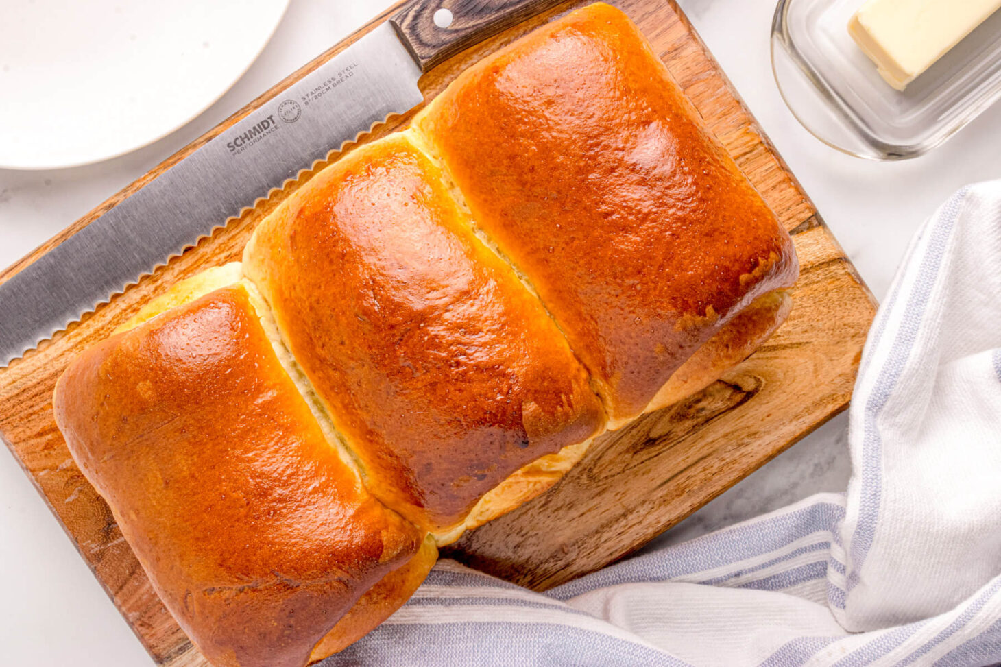 A tri-lobed loaf of golden baked Shokupan, or Japanese Milk bread on a wooden cutting board beside a knife and block of butter.