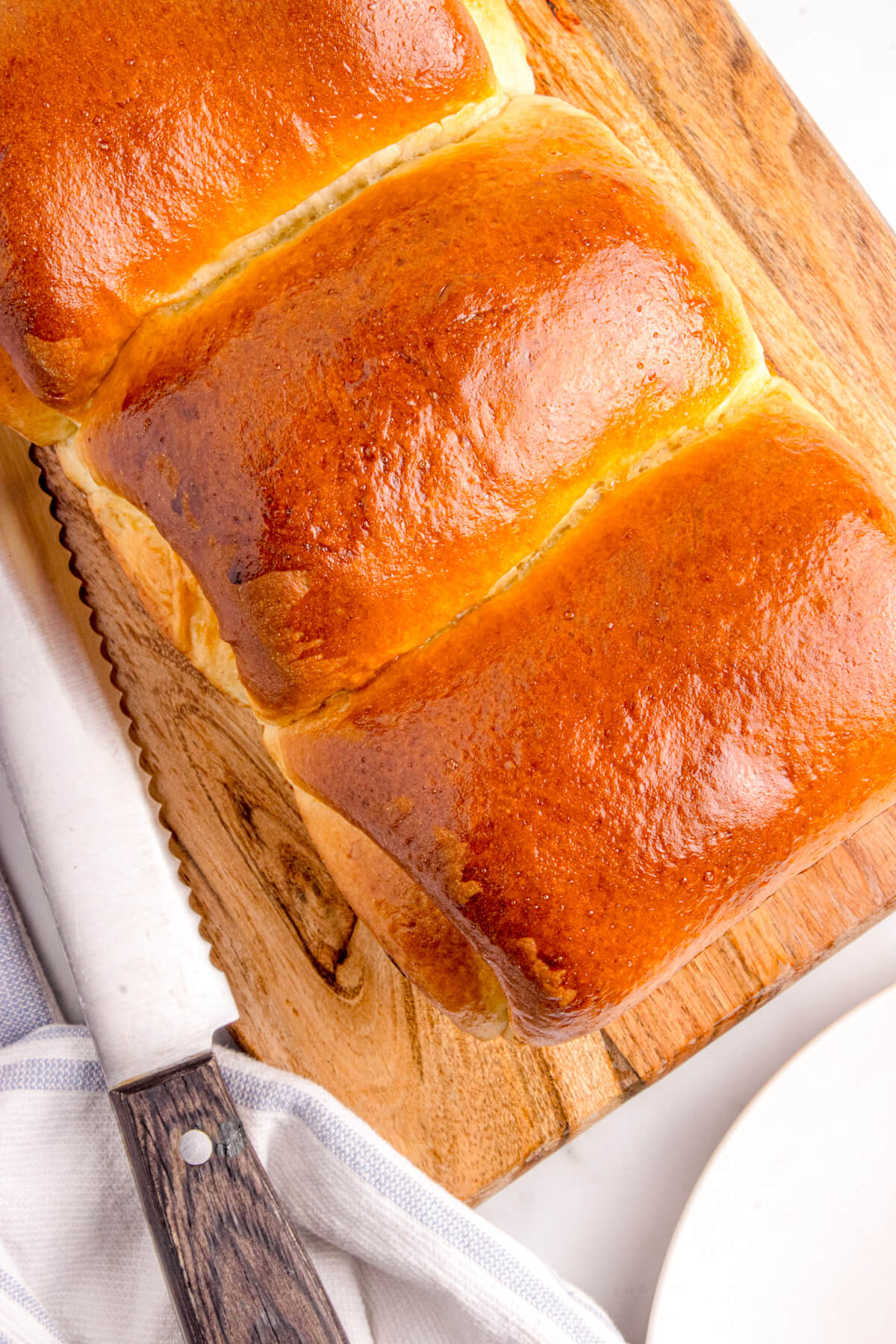 A tri-lobed loaf of golden baked Shokupan, or Japanese Milk bread on a wooden cutting board beside a knife.