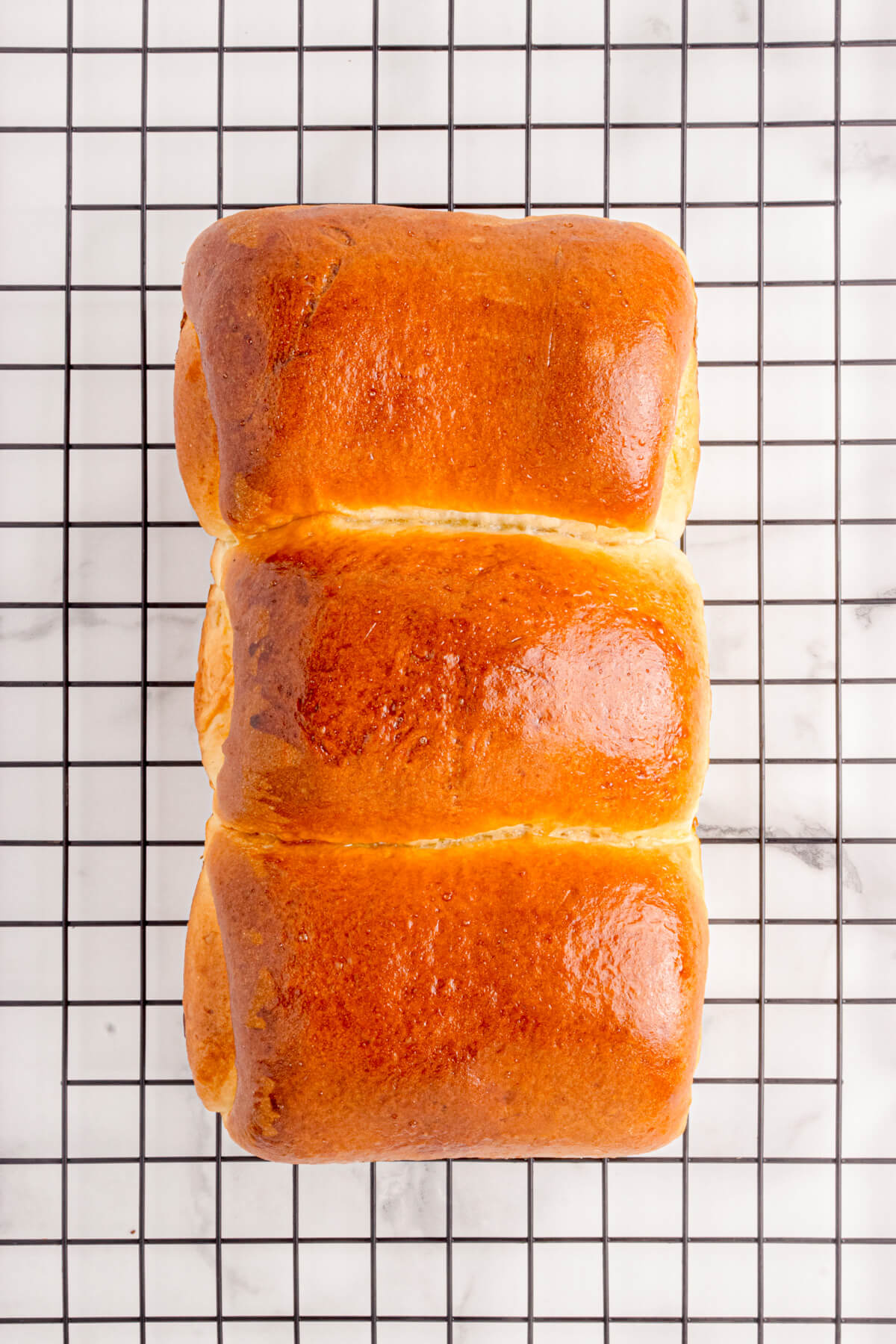 A tri-lobed loaf of golden baked Shokupan, or Japanese Milk bread on a wire cooling rack.