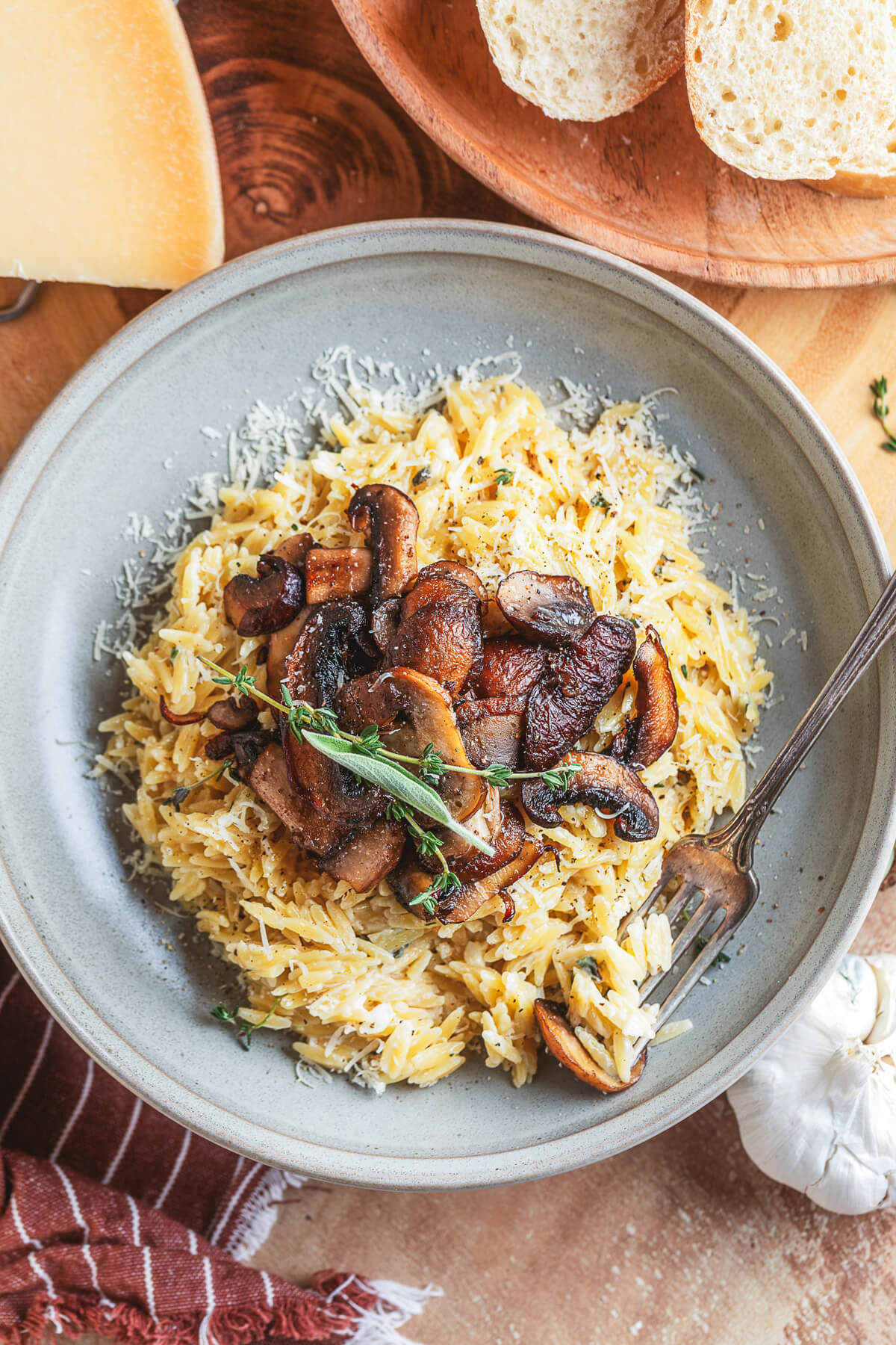 A fork digs into a gray pasta bowl filled with creamy orzo topped with roasted mushrooms and fresh herbs.