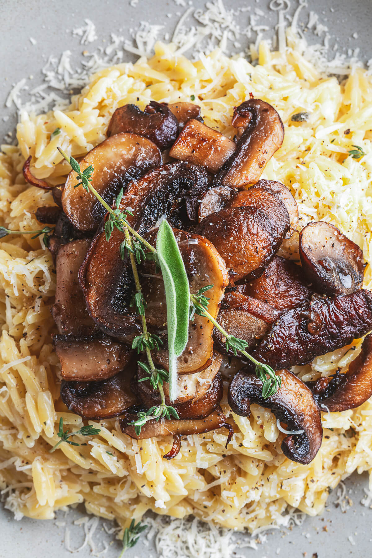 A gray pasta bowl filled with creamy orzo topped with roasted mushrooms and fresh herbs.