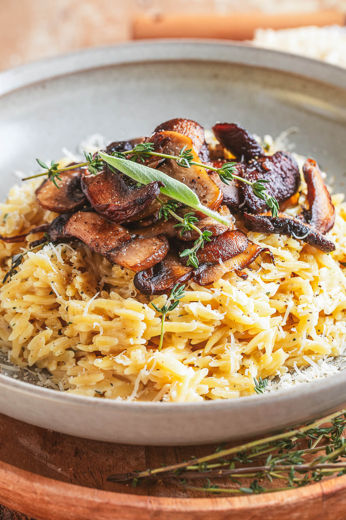 A gray pasta bowl filled with creamy orzo topped with roasted mushrooms and fresh herbs.