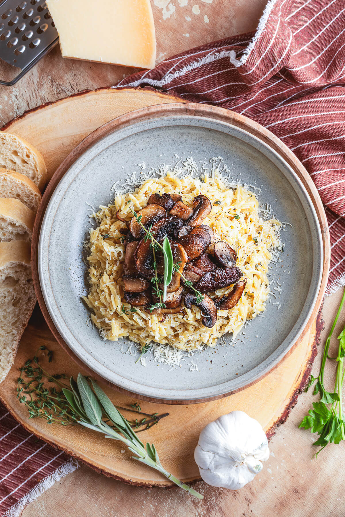 A gray pasta bowl filled with creamy orzo topped with roasted mushrooms and fresh herbs on a dinner table.